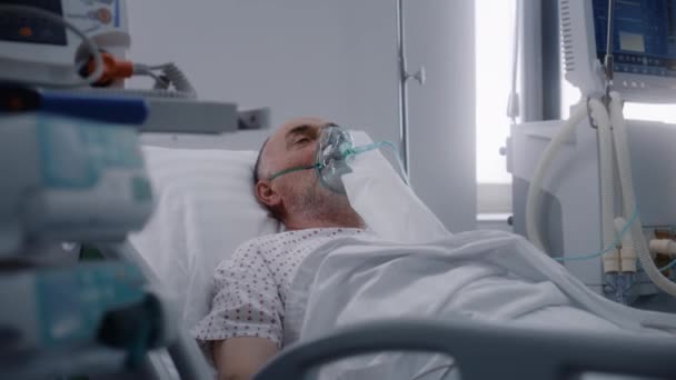 酸素マスクのシニアマンは 病院の病棟のベッドに横たわっています 人工肺換気中の古い患者さん クリニックの緊急治療室 医療施設の集中治療コロナウイルス部門 — ストック動画