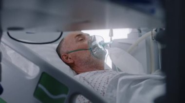 Klinikte modern ekipmanlarla acil servis. Oksijen maskeli yaşlı adam başarılı bir ameliyattan sonra yatakta yatıyor. Hemşire hastayla ilgilenir. Tıbbi tesiste yoğun bakım Coronavirus Bölümü.