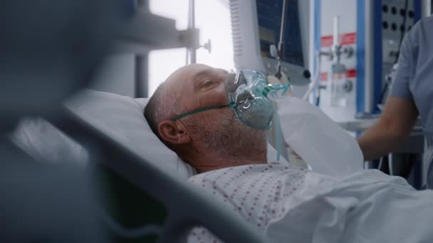 酸素マスクの高齢者は人工肺換気中にベッドに横たわっています 看護師は患者の世話をする 近代クリニックの緊急治療室 医療施設の集中治療コロナウイルス部門 — ストック動画