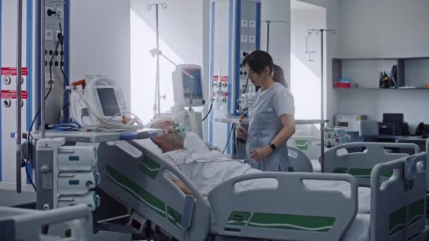 急救室 诊所配备现代化设备 戴氧气面罩的老年人术后躺在床上 友善的护士与老年病人交谈 照顾病人 使用医院监测器 重症监护科 — 图库视频影像