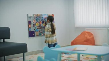 Küçük kız modern hastanenin bekleme salonunda oyuncaklarla eğlence panosuna resim çiziyor. Çocuk klinikte aile doktorundan randevu bekliyor. Çocuk tıbbı ve sağlık hizmetleri kavramı.