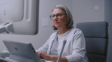 Kadın doktor hastayla konuşur ve ultrason cihazındaki ultrason cihazına bakar. Uzman, gelişmiş ekipmanlarla klinikte prosedürü veya muayeneyi kontrol ediyor.