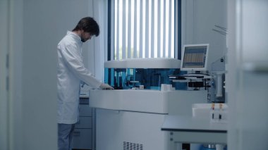 ZAPORIZHYA, UKRAINE - 30 Haziran 2023: Kafkas erkek hemşire kan örnekleriyle birlikte tüpleri biyokimyasal kan testleri için modern otomatik cihaza yerleştirdi. Bilim adamı ya da kimyager biyoteknoloji alanında çalışıyor.