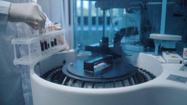 Erkek bilim adamı, biyokimyasal kan testleri için tüp rafından modern otomatik cihaza kan örnekleri koyar. Profesyonel kimyager biyoteknoloji laboratuvarında çalışıyor. Gelişmiş araştırma laboratuvarı.