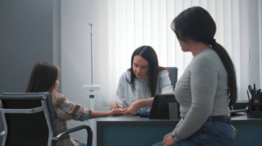 Kadın doktor, endokrinolog modern tıbbi aletler kullanarak hastanedeki genç bir kızın parmağından kan testi yaptırıyor. Asyalı aile ya muayene oluyor ya da klinikte check-up yaptırıyor. Sağlık hizmetleri kavramı.