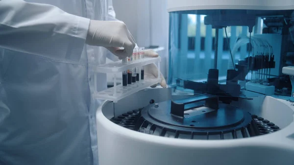 男性の科学者は チューブラックからの血液サンプルを 生化学的血液検査の分析のための現代の自動装置に置きます プロの化学者はバイオテクノロジー研究室で働いています 先進的な研究室 — ストック写真