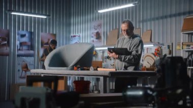 Olgun marangoz veya tasarımcı dijital tablet kullanır ve modern atölyede sandalye ile mobilya yapmak ve yenilemek için çalışır. Bir başka uzman raf montajı yapıyor. El yapımı ve girişimcilik kavramı.