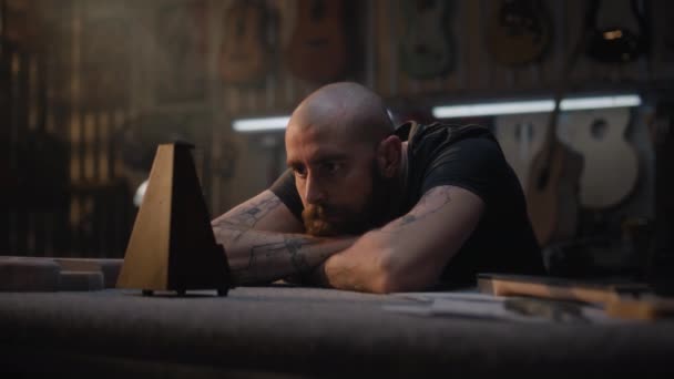 피곤한 장인은 메트로놈을보고 악기를 만들기위한 현대적인 워크샵에 앉아있다 수공예 배경에 — 비디오