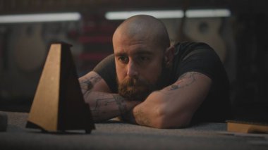 Orta yaşlı dövmeli bir zanaatkar karanlık çalışma odasındaki masada oturur. Profesyonel Kafkasyalı marangoz metronoma bakar ve atölyede uzun bir çalışma gününden sonra dinlenir. El işi ve küçük işletme konsepti.