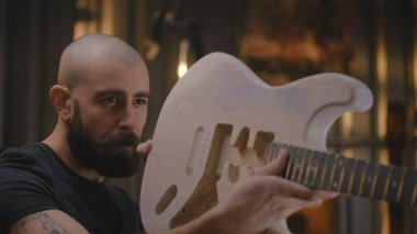 Erkek marangozun cila çektikten sonra gitar boynunu gitar gövdesine yapıştırdığı yakın çekim. Uzman marangoz, zanaatkar modern atölyede müzik aleti yapıyor. El yapımı ve girişimcilik..