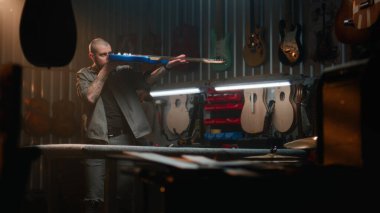 Erkek marangoz gitar tellerini bez parçasıyla siliyor ve gitarı inceliyor. Ahşap ustası, tasarımcı modern atölyede ahşaptan müzik aleti yapıyor. El işi ve küçük işletme konsepti.