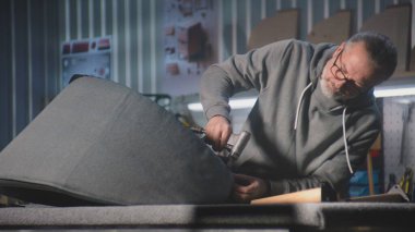 Olgun marangoz zımba tabancasıyla koltuk döşemesini değiştirir. Profesyonel bir zanaatkar, mobilya yapmak için modern ve şık bir atölyede restorasyon yapıyor. El işi ve küçük işletme konsepti.