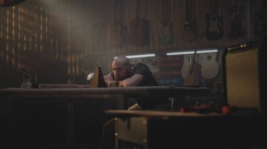 Yorgun marangoz metronoma bakar, müzik aletleri yapmak için atölyeye oturur. Erkek zanaatkar, zanaatkar uzun bir iş gününden sonra rahatlar. Duvarda tahta gitarlar asılı duruyor. El işi ve küçük işletmeler..