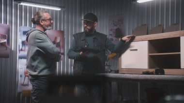 Profesyonel erkek marangoz ya da tasarımcı dijital tablet bilgisayar kullanır, olgun müşterilerle konuşur ve ahşap TV standı yapmayı tartışır. Modern mobilya atölyesi. El yapımı ve girişimcilik kavramı.