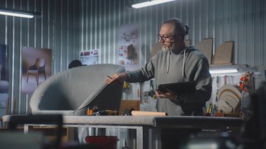 Olgun marangoz veya tasarımcı dijital tablet kullanır ve modern atölyede sandalye ile mobilya yapmak ve yenilemek için çalışır. Bir başka uzman raf montajı yapıyor. El yapımı ve girişimcilik kavramı.