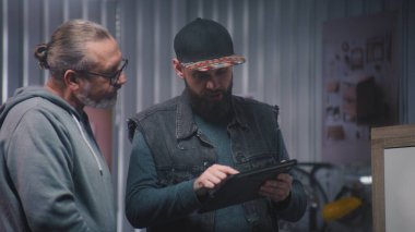 Profesyonel erkek marangoz ya da tasarımcı dijital tablet bilgisayar kullanır, olgun müşterilerle konuşur ve ahşap TV standı yapmayı tartışır. Modern mobilya atölyesi. El işi ve küçük işletme konsepti.