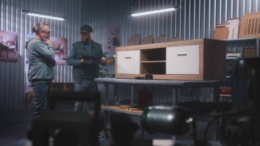 Profesyonel erkek marangoz ya da tasarımcı dijital tablet bilgisayar kullanır, olgun müşterilerle konuşur ve ahşap TV standı yapmayı tartışır. Modern mobilya atölyesi. El yapımı ve girişimcilik kavramı.