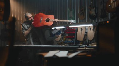 Erkek zanaatkar akustik gitar çalar, sesi kontrol eder. Ahşap ustası, marangoz modern atölyede ahşap müzik aleti yapıyor. Meslektaşlar arka planda çalışır. El yapımı ve girişimcilik..
