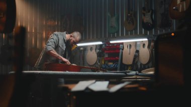 Profesyonel erkek marangoz akustik gitar ve telleri paçavrayla siler. Ahşap işçiliği, ahşap müzik aleti yapar, modern atölyede iş arkadaşıyla çalışır. El yapımı ve girişimcilik..