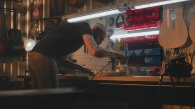 Profesyonel erkek zanaatkar, parlatma makinesi kullanarak tahta gitar gövdesini parlatmış. Ahşap ustası, marangoz modern atölyede müzik aleti yapıyor. El işi ve küçük işletmeler..
