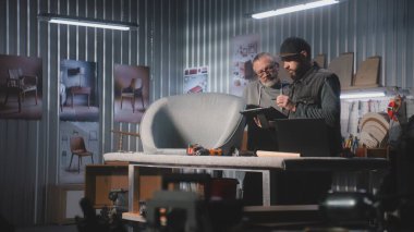 Erkek tasarımcı olgun marangozlarla konuşur, sandalye tasarımı ve üretimi hakkında konuşur, tablet bilgisayar ve dizüstü bilgisayar kullanır. Profesyonel sanatçılar şık mobilya atölyelerinde çalışırlar. El işi ve küçük işletmeler..