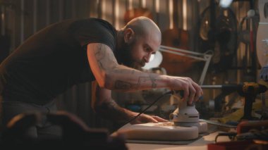 Profesyonel erkek zanaatkar öğütme makinesi kullanarak tahta gitar gövdesini öğütüyor. Ahşap ustası, marangoz modern atölyede müzik aleti yapıyor. El işi ve küçük işletmeler..