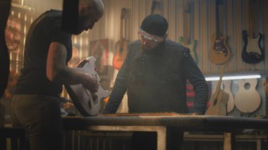 İki profesyonel marangoz, zanaatkarlar tahta gitarın gövdesini inceliyor ve modern atölyede müzik aleti yapma sürecini tartışıyorlar. Meslektaşlar arka planda çalışır. El yapımı ve girişimcilik..