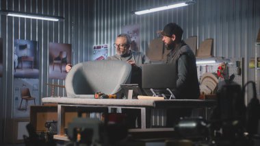 Erkek tasarımcı olgun marangozlarla konuşur, sandalye tasarımı ve üretimi hakkında konuşur, tablet bilgisayar ve dizüstü bilgisayar kullanır. Profesyonel sanatçılar şık mobilya atölyelerinde çalışırlar. El işi ve küçük işletmeler..