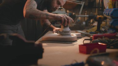 Profesyonel erkek marangoz parlatma makinesi kullanarak tahta gitar gövdesini parlatmış. Ahşap ustası, zanaatkar modern atölyede müzik aleti yapıyor. El yapımı ve girişimcilik..