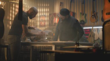 İki profesyonel marangoz, zanaatkarlar tahta gitarın gövdesini inceliyor ve modern atölyede müzik aleti yapma sürecini tartışıyorlar. Meslektaşlar arka planda çalışır. El yapımı ve girişimcilik..