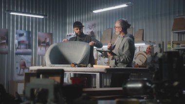 Olgun marangoz ya da tasarımcı dijital tablet bilgisayar kullanarak sandalye yapımı için hesaplamalar yapar, erkek meslektaşlarıyla istişarelerde bulunur. Sanatçılar modern mobilya atölyesinde çalışırlar. El yapımı ve girişimcilik.