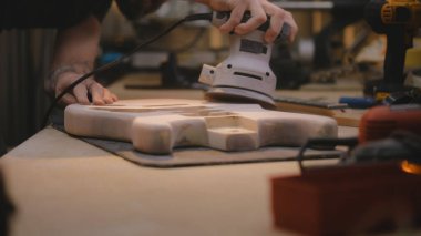Erkek marangozun, iş yerindeki tahta gitar vücudunu parlatırken yakın plan fotoğrafı. Ahşap ustası, zanaatkar modern atölyede müzik aleti yapıyor. El yapımı ve girişimcilik..