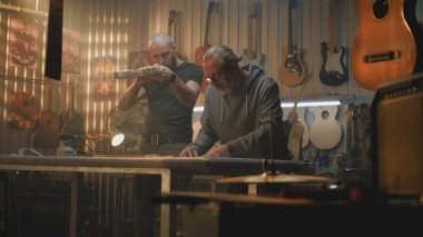 İki profesyonel marangoz ahşap gitar yapar ve ölçü alır. Modern atölyede müzik aletleri yapan sanatçılar. İş arkadaşı arka planda çalışıyor. El yapımı ve girişimcilik..