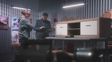 Profesyonel erkek marangoz ya da tasarımcı, dijital tablet bilgisayarı ile olgun iş arkadaşlarıyla konuşur ve ahşap TV standı yapmayı tartışır. Modern mobilya atölyesi. El işi ve küçük işletme konsepti.