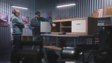 Profesyonel erkek marangoz ya da tasarımcı dijital tablet bilgisayar kullanır, olgun müşterilerle konuşur ve ahşap TV standı yapmayı tartışır. Modern mobilya atölyesi. El yapımı ve girişimcilik kavramı.