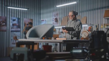 Olgun marangoz veya tasarımcı dijital tablet kullanır ve modern atölyede sandalye ile mobilya yapmak ve yenilemek için çalışır. Bir başka uzman raf montajı yapıyor. El yapımı ve girişimcilik kavramı.