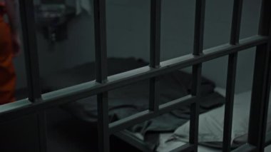 Turuncu üniformalı suçlu hapishane yatağında yatıyor. Mahkum, suçtan hapis cezasına çarptırıldı. Islah evindeki tutuklu. Adalet sistemi. Metal parmaklıklardan bak. Kapat..
