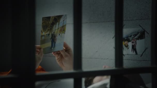 男囚犯看着躺在床上的照片 牢房的墙上挂着家人的照片 被非法定罪的人在狱中服刑 拘留中心或教养所 — 图库视频影像