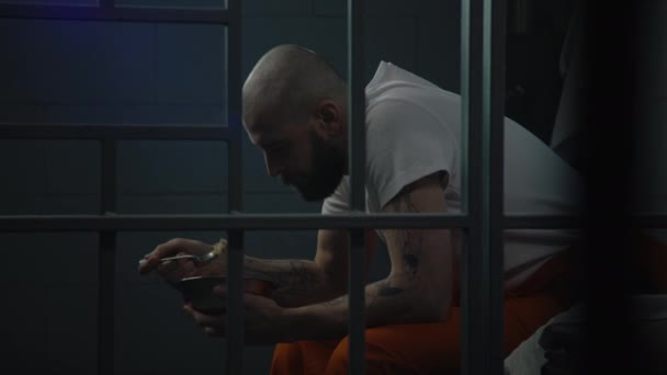 Muž Oranžové Uniformě Sedí Posteli Vězeňské Cele Nechutné Vězeňské Jídlo — Stock video
