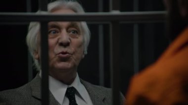 Avukat, hapishane hücresinde duran turuncu üniformalı bir suçluyla konuşuyor ve hizmetlerini sunuyor. Mahkûm, ıslah evinde hapis yatıyor. Tutukevinde ya da hapiste. Kapat..