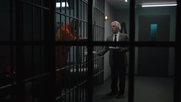 Kriminálník Oranžové Uniformě Opírá Vězeňské Mříže Mluví Obhájcem Čte Jeho — Stock video