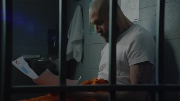 Ein Deprimierter Männlicher Häftling Orangefarbener Uniform Betrachtet Seine Kinderzeichnungen Und — Stockvideo