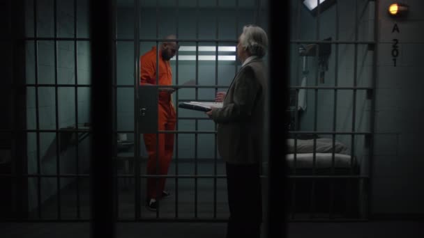 Więzień Pomarańczowym Mundurze Chodzi Kratkami Celi Rozmawia Adwokatem Czyta Umowę — Wideo stockowe