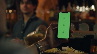 Yeşil ekranlı telefonu tutan adamın görüntüsü, ekrana dokunuyor. Spor fanatiği bahisçilerin reytinglerini internetten izliyor ya da internette sörf yapıyor, barmenle barda oturuyor. Krom anahtar.