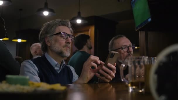 Dwóch Przyjaciół Ogląda Mecz Piłki Nożnej Żywo Telewizji Siedząc Barze — Wideo stockowe