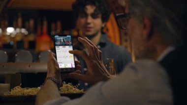 Spor taraftarlarının maç skorlarını ve cep telefonu kullanarak bahisçi reytinglerini kapat. Beyaz adam, geceleri barın barında oturarak futbol dünya ligi maçına bahis oynuyor. Kumar konsepti.