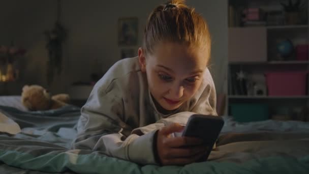 通过手机与朋友视频聊天的年轻女孩的亲密接触 白人青少年躺在舒适的床上 迷人的少女在家里的舒适卧室度过周末 — 图库视频影像