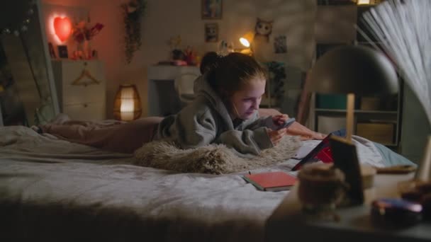 白人青少年用她的手机上网 在社交网络上与朋友聊天 小女孩躺在舒适的大床上 晚上休息 孩子们常呆在家里舒适的卧室里 — 图库视频影像