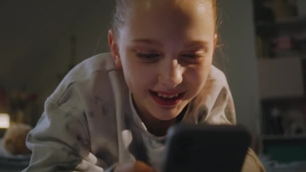 傍晚时分 一个白人少年躺在舒适的床上 躺在她舒适的卧室里 小女孩用她的手机和朋友通过视频聊天 有魅力的青少年周末呆在家里 — 图库视频影像