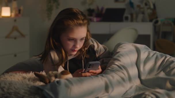 小女孩躺在舒适的卧室里睡觉 白人青少年利用智能手机上网 深夜在社交网络上与朋友聊天 十几岁的孩子在家里的房间里度过周末 — 图库视频影像